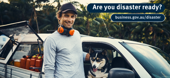 Image of a tradesman standing by ute ute, his working dog is inside the cabin and the back is filled  with jerry cans and tools. He is in a tropical setting.