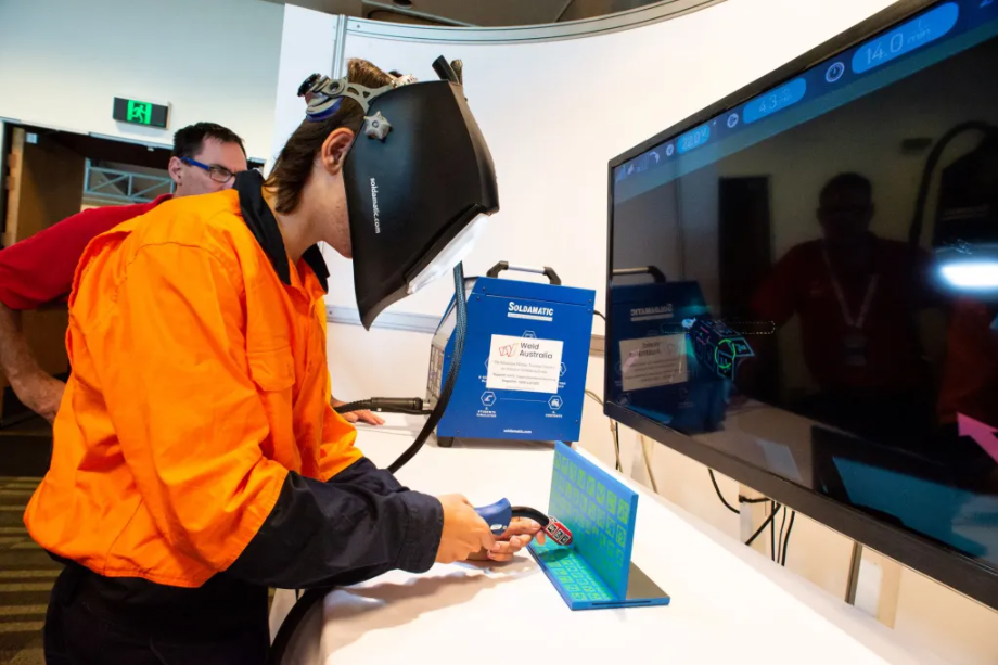 A image of a man in orange hi-vis wearing a welding helmet at an ex display