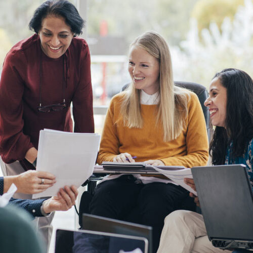 Three people gathered around a piece of paper smiling. Two are seated, one is standing.