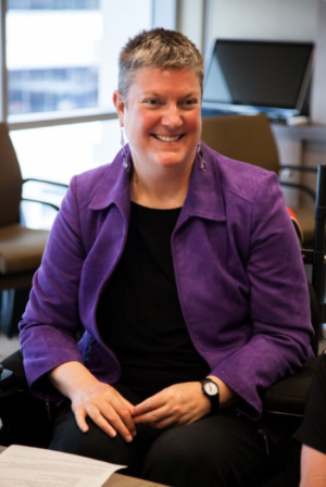Christina Ryan smiling in a purple jacket. Christina is a white woman with short grey hair.