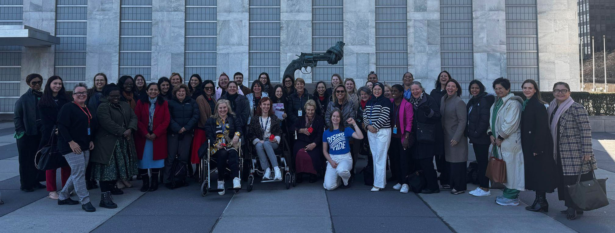 Australia's delegation to CSW69 standing together in front of The Knotted Gun sculpture at the UN Headquarters in New York
