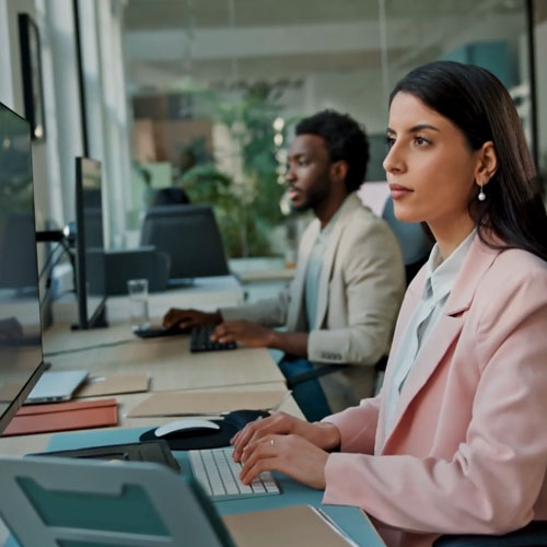 A women and a man at a shared desk typing and looking at a computer screen. 