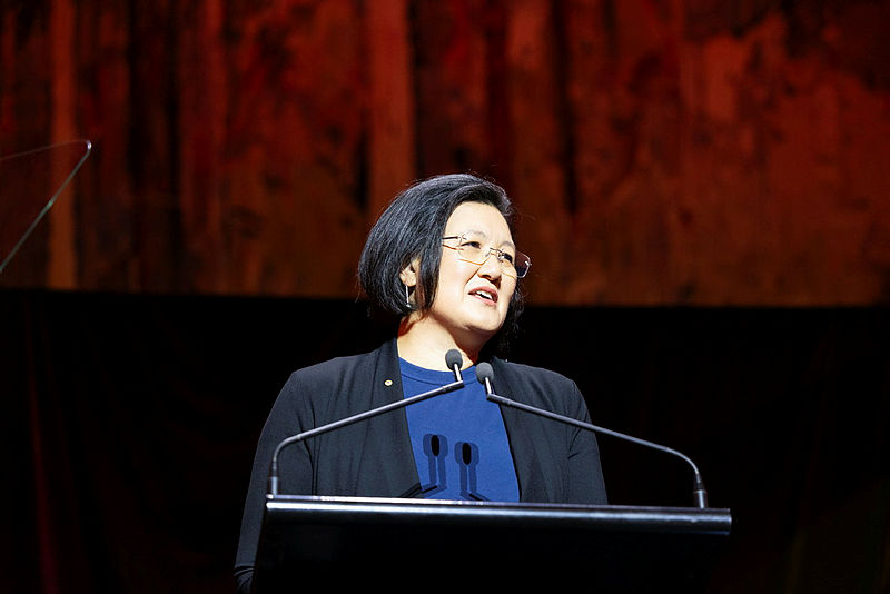 Ming Long speaking on stage at the Wang Gungwu lecture. Ming is a Chinese Australian woman with short black hair, wearing glasses and professional attire