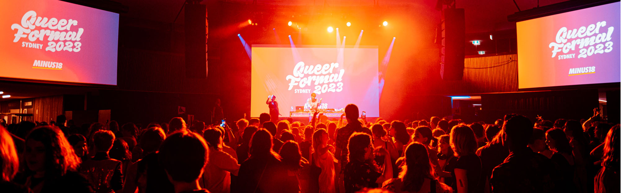 Night club with orange lighting, people dancing in front of a DJ on stage, and three screens that say 'Queer Formal Sydney 2023'