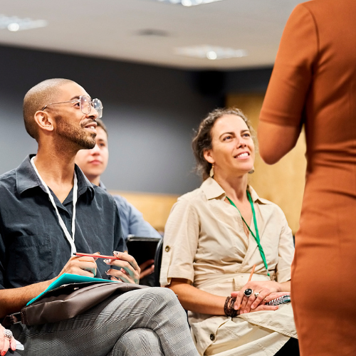 Three seated attendees looking at a speaker. Only half of the back of the speaker is visible