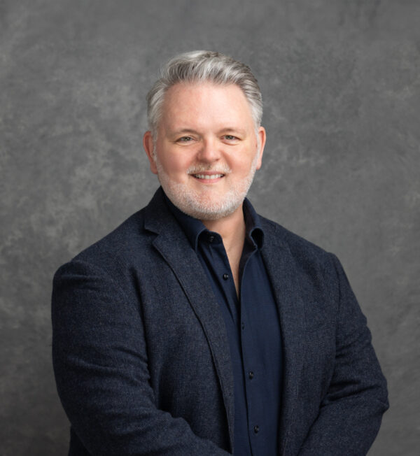 Terence Humphreys in a black suit against a grey background.